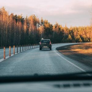 A car driving through a winding road surrounded by forest trees during sunset, creating a tranquil travel scene.